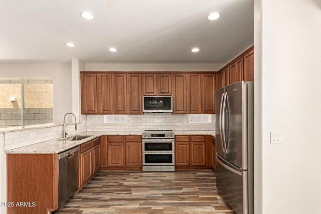17493 N Costa Brava Ave, Maricopa, AZ 85139 - kitchen featuring appliances with stainless steel finishes, brown cabinetry, wood finished floors, light stone counters, and tasteful backsplash