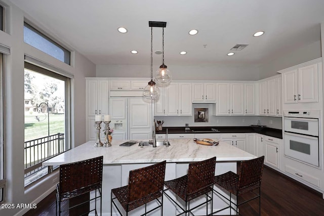 kitchen featuring paneled built in refrigerator, white double oven, dark wood-style flooring, and white cabinetry