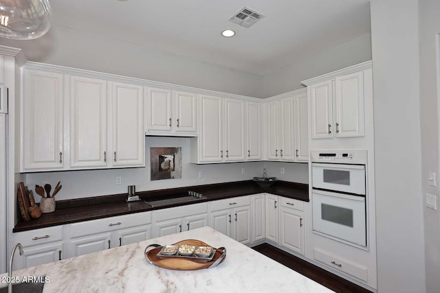 kitchen with double oven, white cabinets, visible vents, and black electric stovetop