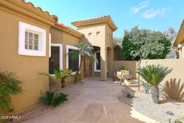 property entrance featuring a tiled roof, a patio area, fence, and stucco siding