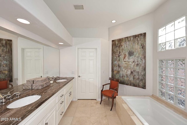 bathroom with double vanity, a garden tub, a sink, and recessed lighting