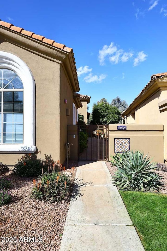 view of property exterior featuring a tile roof, a gate, and stucco siding