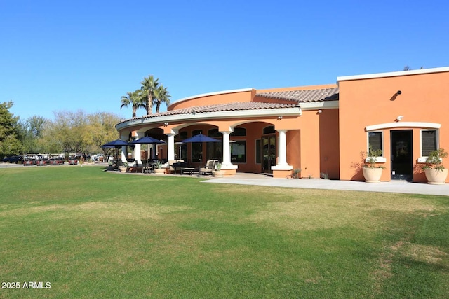 back of property featuring a tile roof, a yard, and stucco siding