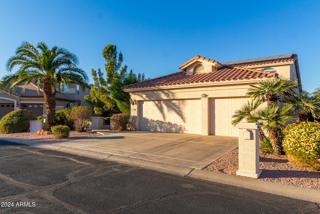 mediterranean / spanish-style home with driveway, a tile roof, roof mounted solar panels, and stucco siding