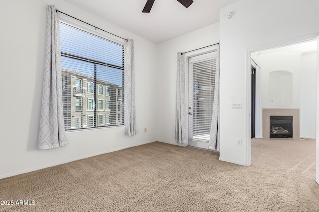 unfurnished room featuring carpet flooring, ceiling fan, and a tiled fireplace