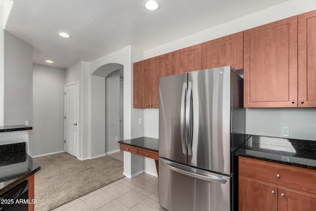 kitchen with dark stone counters, stainless steel refrigerator, and light colored carpet