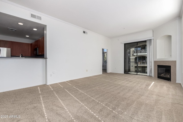 unfurnished living room with a tile fireplace, carpet, and ornamental molding