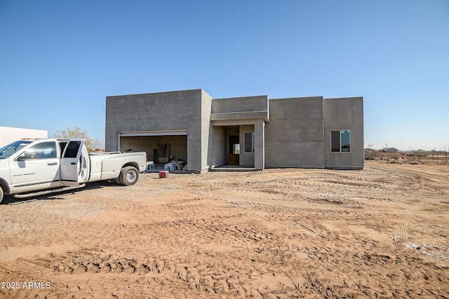 view of front of house featuring a garage, dirt driveway, and stucco siding