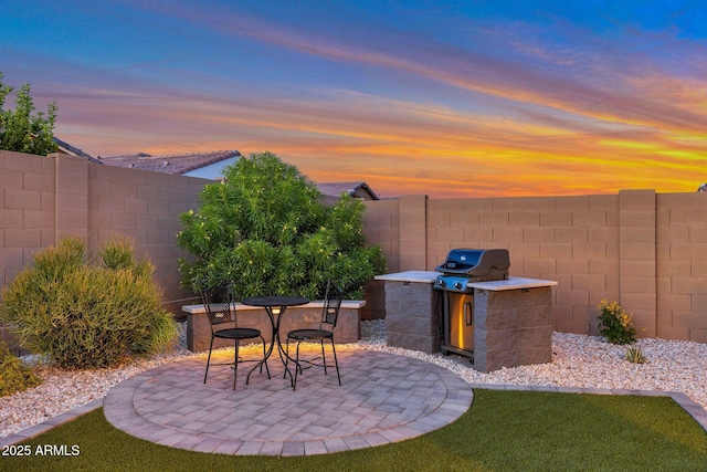 19908 W Montecito Ave, Litchfield Park, AZ 85340 - patio terrace at dusk with a patio, a fenced backyard, and exterior kitchen