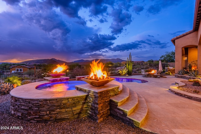 pool at dusk with a mountain view, an outdoor fire pit, an outdoor hot tub, and a patio area