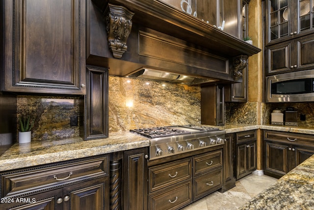 kitchen with backsplash, stainless steel appliances, light tile floors, light stone counters, and dark brown cabinetry