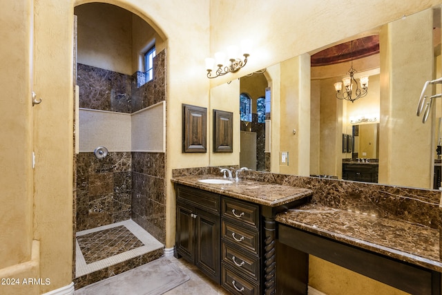 bathroom featuring vanity with extensive cabinet space, an inviting chandelier, tiled shower, and tile flooring