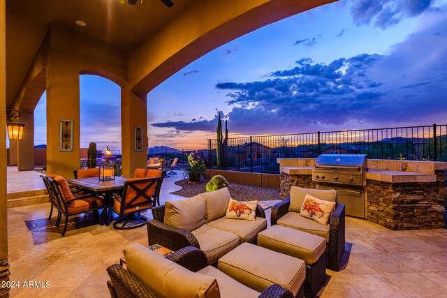 patio terrace at dusk featuring exterior kitchen, area for grilling, and an outdoor living space