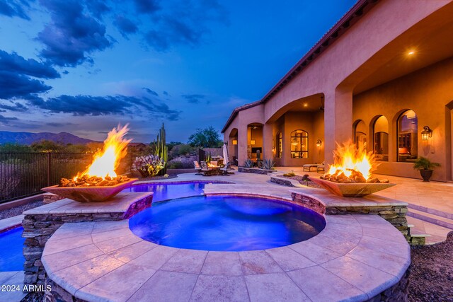 pool at dusk with an outdoor fire pit, an in ground hot tub, and a patio area