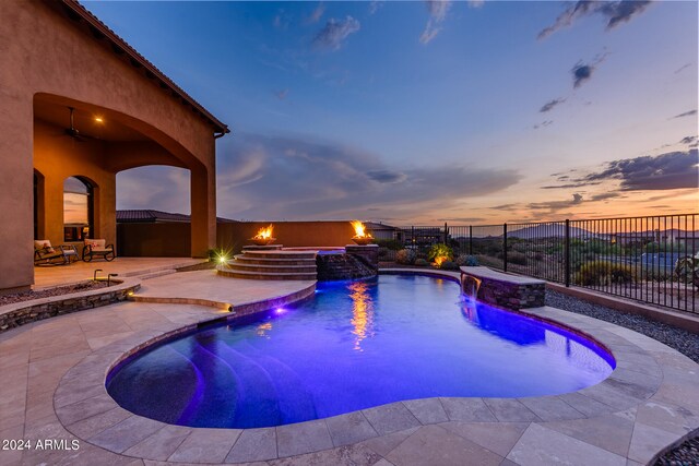 pool at dusk with a patio area, pool water feature, and an outdoor hot tub