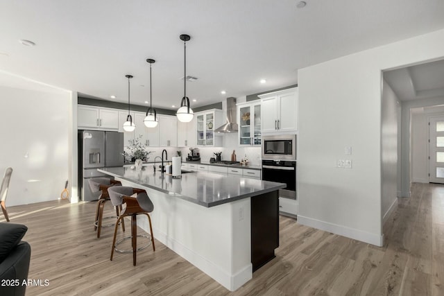 kitchen featuring wall chimney exhaust hood, sink, white cabinetry, stainless steel appliances, and a kitchen island with sink