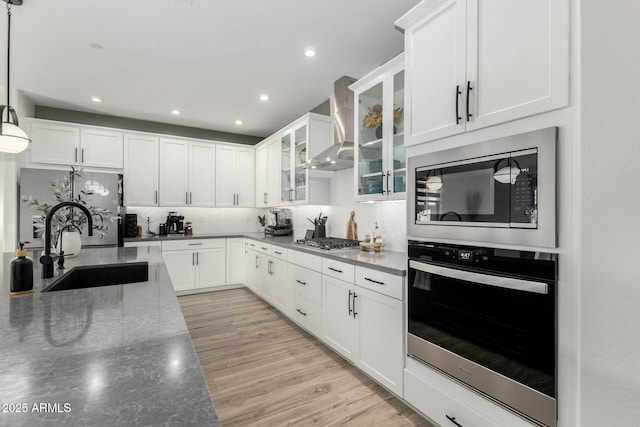 kitchen featuring pendant lighting, sink, dark stone countertops, stainless steel appliances, and wall chimney exhaust hood