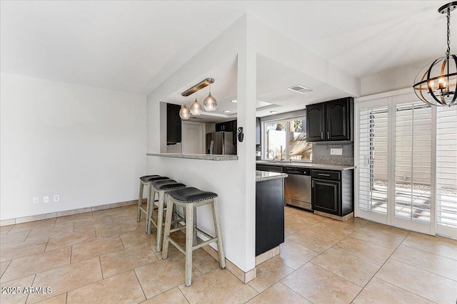 kitchen with appliances with stainless steel finishes, an inviting chandelier, decorative backsplash, a kitchen breakfast bar, and light tile patterned floors