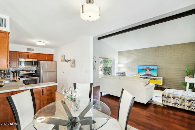 dining area with brick wall, lofted ceiling with beams, wood-type flooring, and sink