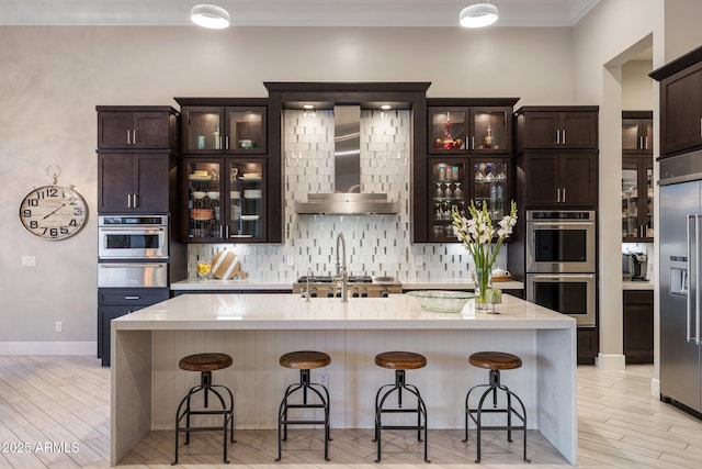 kitchen with stainless steel appliances, light wood-style floors, a warming drawer, wall chimney exhaust hood, and tasteful backsplash