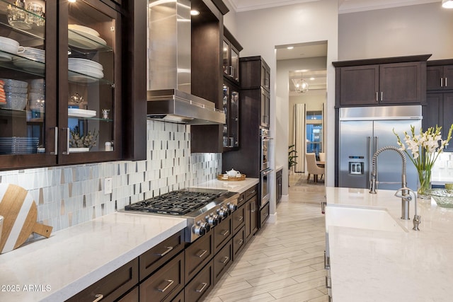 kitchen with crown molding, stainless steel appliances, tasteful backsplash, wall chimney range hood, and dark brown cabinets