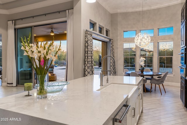 kitchen featuring light stone counters, a ceiling fan, white cabinets, hanging light fixtures, and light wood finished floors