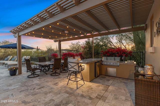 patio terrace at dusk with exterior kitchen, outdoor dining space, area for grilling, and a pergola