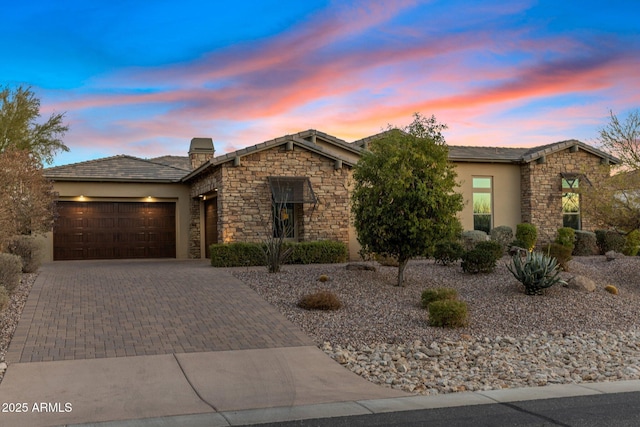 view of front facade featuring an attached garage, stone siding, decorative driveway, stucco siding, and a chimney