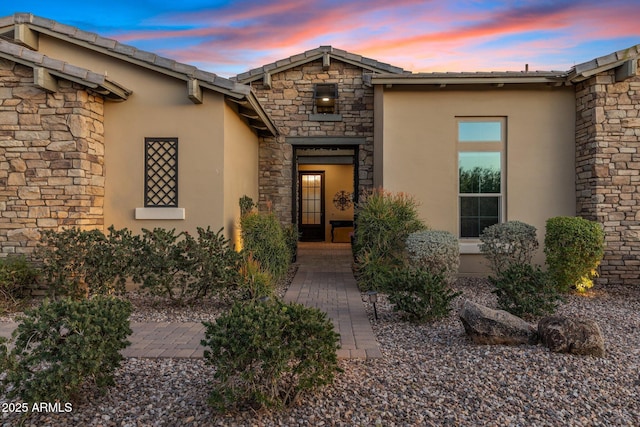 exterior entry at dusk featuring stone siding and stucco siding