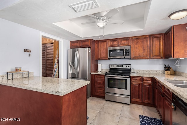 kitchen featuring appliances with stainless steel finishes, light stone countertops, a tray ceiling, and light tile patterned floors