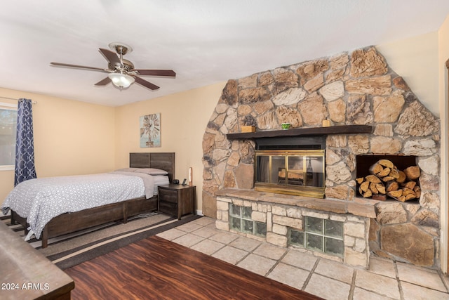 bedroom featuring light hardwood / wood-style floors, a stone fireplace, and ceiling fan