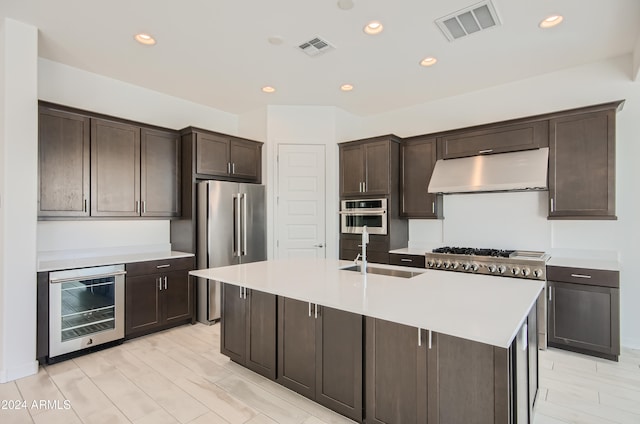 kitchen featuring sink, beverage cooler, a kitchen island with sink, dark brown cabinets, and appliances with stainless steel finishes