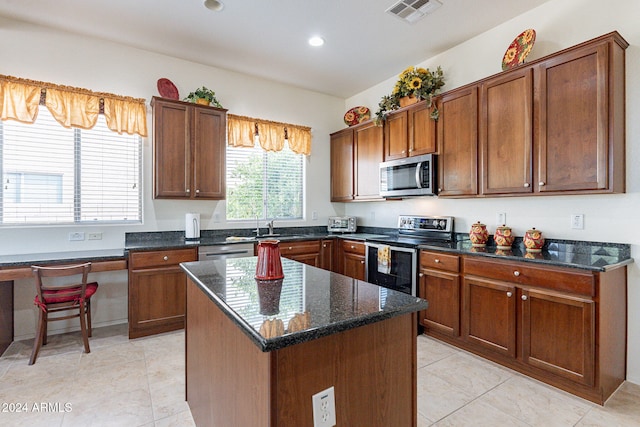 kitchen with light tile patterned flooring, sink, appliances with stainless steel finishes, dark stone countertops, and a kitchen island