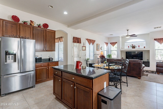 kitchen with light tile patterned flooring, ceiling fan, a kitchen island, dark stone countertops, and stainless steel fridge