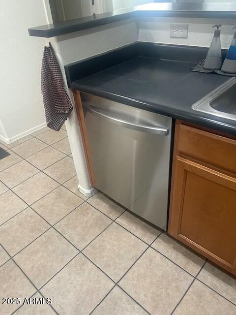 kitchen with light tile patterned floors, brown cabinets, dark countertops, and stainless steel dishwasher