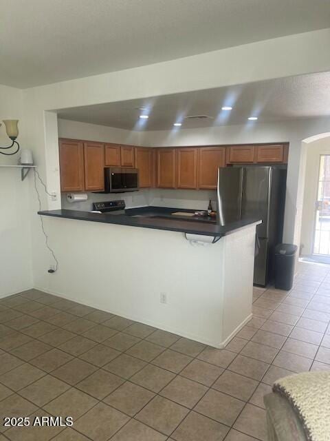 kitchen featuring dark countertops, light tile patterned floors, brown cabinets, and appliances with stainless steel finishes