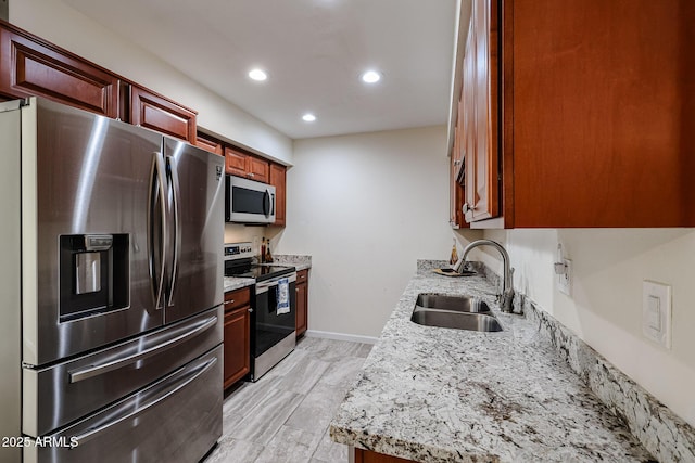 kitchen featuring recessed lighting, stainless steel appliances, baseboards, a sink, and light stone counters