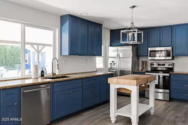 kitchen featuring appliances with stainless steel finishes, dark wood-type flooring, blue cabinetry, hanging light fixtures, and sink