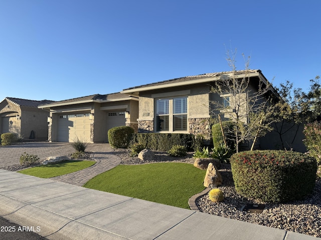 prairie-style house with a front lawn, stucco siding, decorative driveway, stone siding, and an attached garage