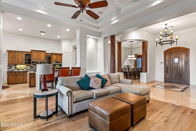 living room with ceiling fan with notable chandelier, light wood-type flooring, a towering ceiling, and ornate columns