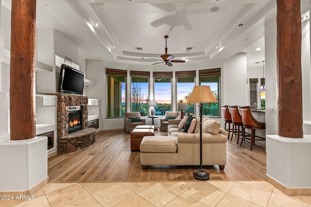 tiled living room featuring a tray ceiling, ornate columns, ceiling fan, and a fireplace