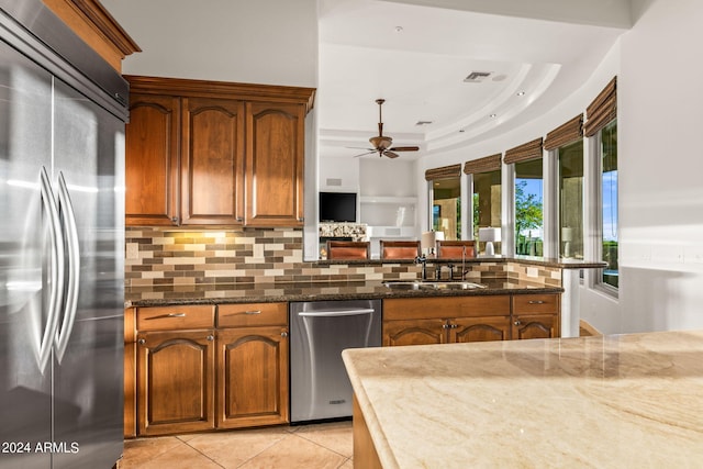 kitchen with decorative backsplash, a raised ceiling, appliances with stainless steel finishes, and dark stone counters