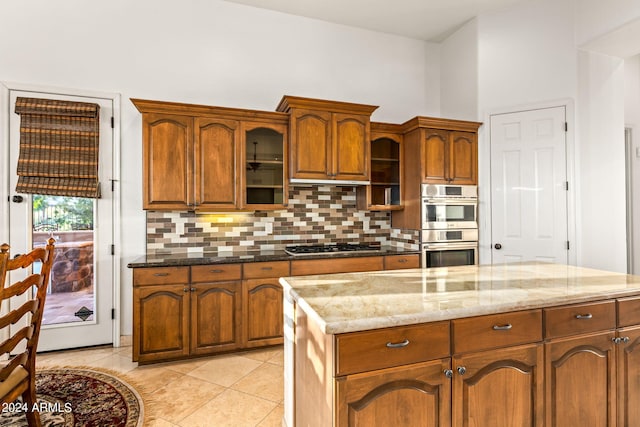 kitchen with tasteful backsplash, light stone countertops, light tile patterned floors, and appliances with stainless steel finishes