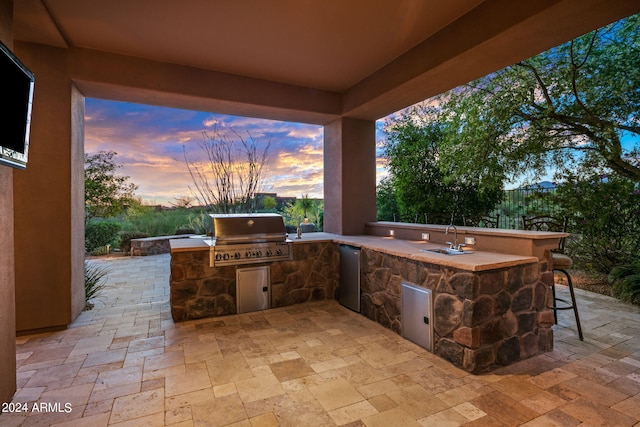 patio terrace at dusk featuring a grill, exterior kitchen, and an outdoor wet bar