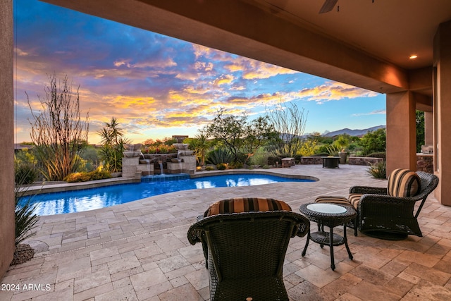 pool at dusk with a patio area, a jacuzzi, pool water feature, and a mountain view