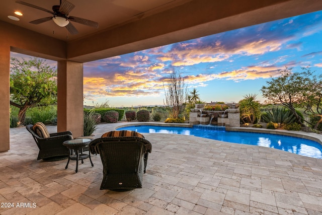 pool at dusk featuring ceiling fan and a patio