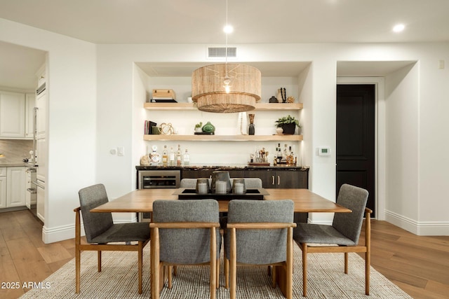 dining area with light wood-style flooring, a dry bar, visible vents, and baseboards