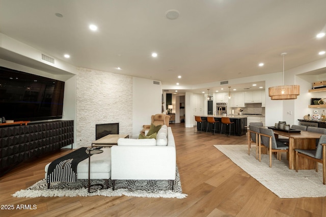 living room featuring light wood-type flooring, recessed lighting, visible vents, and a stone fireplace