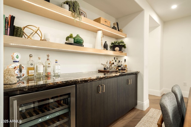 bar with light wood-style flooring, recessed lighting, beverage cooler, baseboards, and a bar