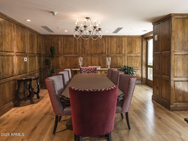 dining space featuring an inviting chandelier, light wood-style flooring, visible vents, and wood walls